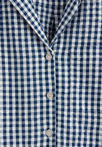 Koszula w niebiesko-białą kratkę z kołnierzykiem, sześcioma guzikami i kieszonką z przodu. Materiał wydaje się lekki i teksturowany.