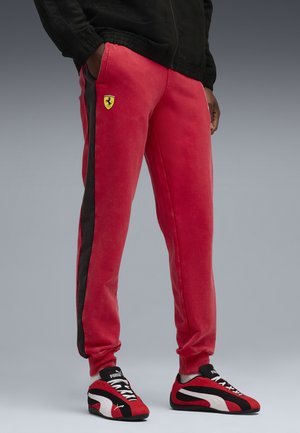 Røde fleece joggere med sort side-stribe og Ferrari-logo. Har elastisk talje og manchetter, parret med sorte og røde sneakers.