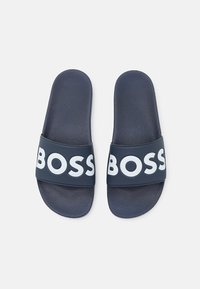 Sötétkék csúszópapucsok texturált talprésszel és széles pánttal, melyen hangsúlyos fehér "BOSS" logó található. Műanyagból készült.