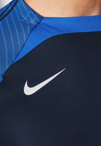 Nike träningströja med en mörk marinblå botten, blå mönstrad yoke och en vit swoosh-logotyp på bröstet. Slät tygkvalitet.