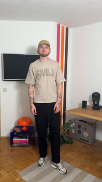 Bež majica s natpisom "FAVELA" u tamnijoj bež boji, crne hlače, sive tenisice i svijetlosmeđa kapa. Unutarnji prostor s šarenim prugama.