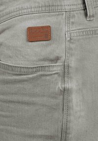 Lys grå denimjeans med en teksturert finish og en synlig oransjebrun lærmerke merket "BLEND" på baklommen.