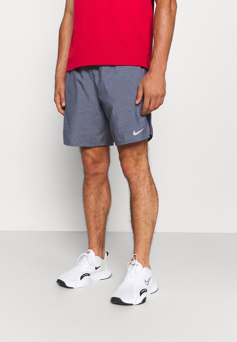 Grijze sportshorts gemaakt van lichtgewicht stof, met een contrasterend zwart Nike-logo. Gecombineerd met witte sneakers en een rood shirt.