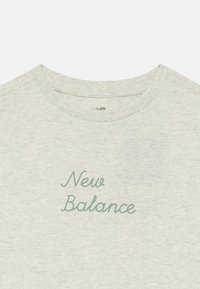 T-shirt gris clair à col rond avec le texte "New Balance" en cursive verte centré sur la poitrine.