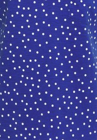 Blue fabric featuring white polka dots of varying sizes, smooth texture, and a small pocket detail on the right side.