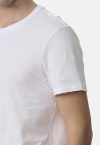 Biała bawełniana koszulka z krótkim rękawem i okrągłym dekoltem. Materiał ma gładką teksturę i jest lekko dopasowany w kształcie.