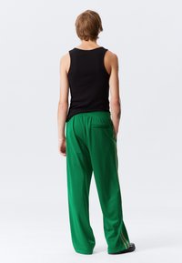 Groene trainingsbroek met een losse pasvorm, elastische tailleband, twee achterzakken en strepen aan de zijkanten. Gecombineerd met een zwart mouwloos topje.