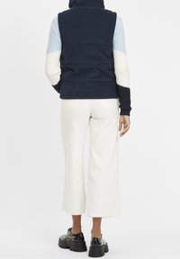 Marinblå manchesterväst med hög krage och randiga ärmar i ljusblått och krämvitt. Kombinerad med vita vida byxor och svarta skor.