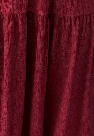 Tissu rouge profond avec une texture froissée, rassemblé en plis verticaux créant une apparence fluide et superposée.