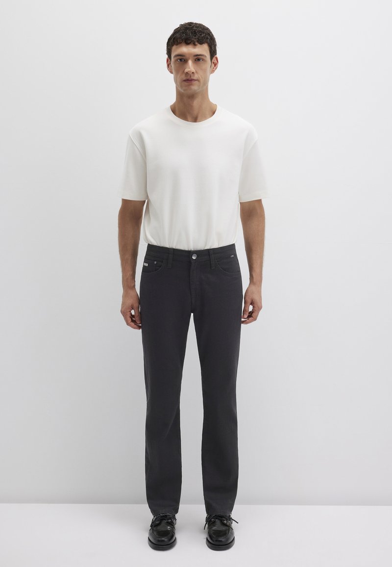 Weißes T-Shirt mit kurzen Ärmeln, kombiniert mit dunkelgrauen geraden Hosen. Das T-Shirt hat eine glatte Textur, während die Hose einen Knopfverschluss und Taschen hat.