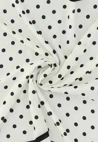 Biały materiał w czarne kropki, o miękkiej strukturze i spiralnym układzie. Krawędzie obramowane czarną bordiurą.