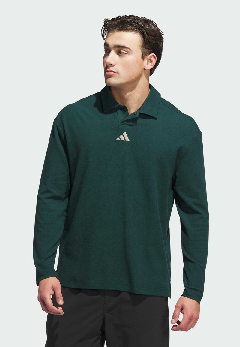 Dark green long-sleeve polo shirt with a collar, featuring a small light grey Adidas logo on the chest and a smooth fabric texture.