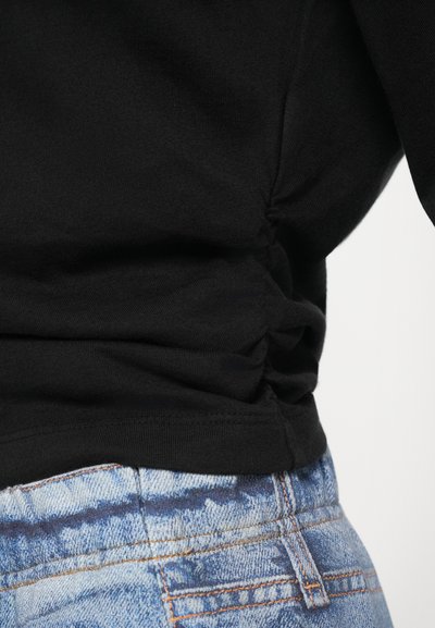 Svart ribbet topp med samlet sidesøm, kombinert med lyseblå denimjeans med et falmet mønster og oransje søm.