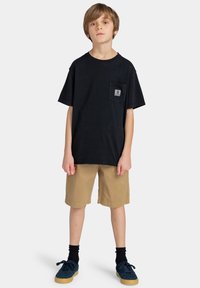 Zwart katoenen T-shirt met een borstzak, gecombineerd met kaki shorts. Zwarte sokken en blauwe schoenen maken de look compleet. Eenvoudig ontwerp en neutrale kleuren.