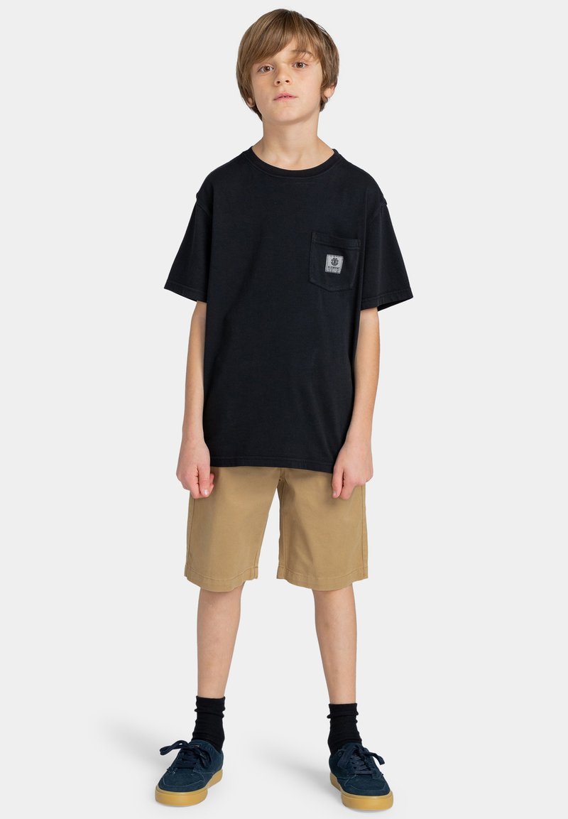 Zwart katoenen T-shirt met een borstzak, gecombineerd met kaki shorts. Zwarte sokken en blauwe schoenen maken de look compleet. Eenvoudig ontwerp en neutrale kleuren.