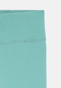 Leggings de sport taille haute sans coutures en bleu sarcelle clair avec des détails de couture à plat visibles sur un fond blanc.