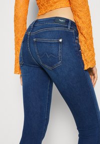 Vaqueros de mezclilla azul oscuro con un corte slim. Cuenta con una etiqueta de cuero en la cintura y dos bolsillos traseros con detalles bordados.