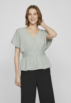 Világoszöld peplum blúz V nyakkal, rövid ujjakkal, gombos záródással és elasztikus derékrésszel. Simább anyag, enyhe eséssel. Fekete nadrággal párosítva.
