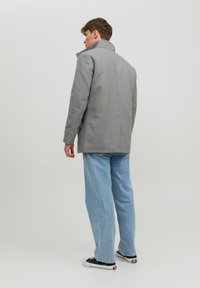 Grå uldblandingsfrakke med høj krave, flade skuldre og lige pasform, parret med lyseblå jeans og sorte sneakers.