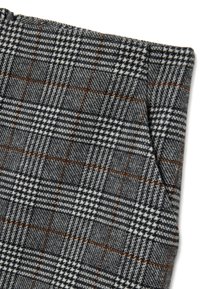 Grau-weißer Hahnentrittstoff mit braunen und schwarzen Akzenten, der eine strukturierte Webart und ein sichtbares Taschen-Detail aufweist.