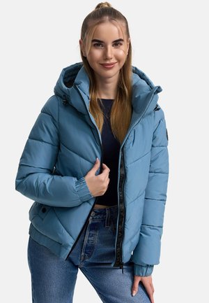 Giacca imbottita azzurro chiaro con cappuccio, con polsini a coste e zip nera. Indossata con una maglietta aderente e jeans a vita alta.