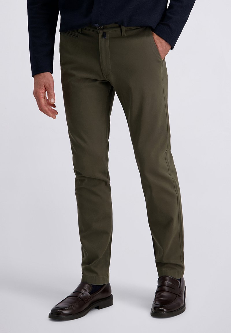 Olijfgroene chino's met een slanke pasvorm, voorzien van zijzakken en een subtiele glans, gecombineerd met donkerbruine loafers. Gladde stoftextuur.