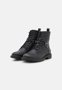 Botas de cuero negro hasta el tobillo con cordones, superficie texturizada, punta redonda y un acento lateral en oro rosa. Suelas de goma con patrones de tracción.