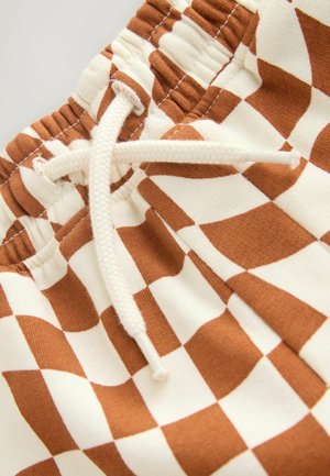 Detailný záber na hnedobielu kockovanú látku s elastickým pásom a bielou šnúrkou zviazanou do uzla.