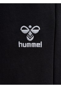 Crni materijal glatke teksture s izvezenim bijelim logotipom pčele i nazivom marke "hummel" ispod.