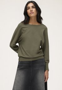 Pulover ușor, de culoare verde măsliniu, cu mâneci lungi și un decolteu larg, asortat cu o fustă A-line din denim închis. Textură netedă și moale.