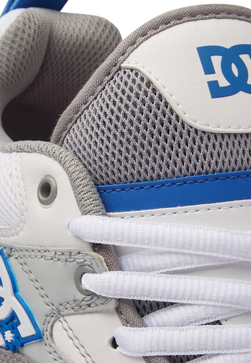 Weiße und graue Sneaker aus Mesh- und Leder-Materialien, mit blauen Akzenten und flachen weißen Schnürsenkeln, versehen mit einem Logo an der Seite.