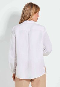 Camicia bianca a maniche lunghe con yoke sulla schiena, aperture laterali, polsini con bottoni e vestibilità rilassata, realizzata in tessuto leggero.