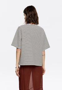 Chemise à rayures à manches courtes en noir et blanc, dotée d'une coupe décontractée et d'un col rond. Portée avec une jupe superposée marron.