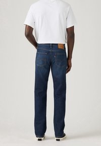 Mörkblå denimjeans med rak benpassform, utrustade med en läderlapp på baksidan, sömmar på bakfickorna och en subtil urblekt textur.