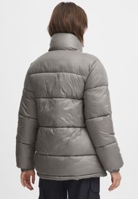 Grå puffjacka med hög krage, horisontellt quiltat mönster och elastiska ärmar. Slät, glänsande textur med en avslappnad passform.