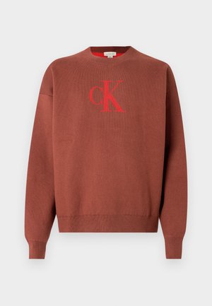 Camisola castanha de malha com gola redonda, apresentando um logótipo "CK" vermelho na parte da frente. Punhos e bainha canelados, textura lisa.