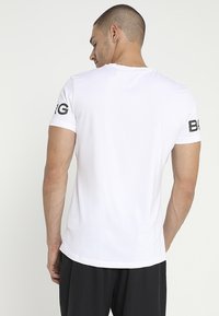 Camiseta deportiva blanca de manga corta, con una textura suave y detalle del logo negro en la manga izquierda.