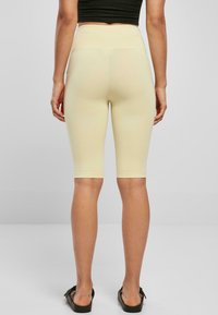 Hoge taille fietsbroek in lichtgeel, met een gladde, rekbare stof die tot halverwege de kuit reikt en een getailleerd ontwerp heeft.