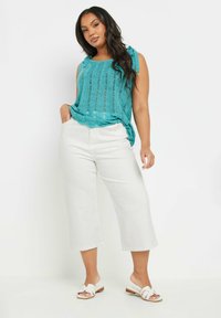 Turkoosi neuleliivi avoimien silmukoiden designilla, yhdistettynä valkoisiin leveälahkeisiin housuihin. Ominaisuuksiin kuuluu olkahihnat ja rento istuvuus. Asusteina valkoiset sandaalit.