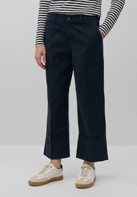 Pantaloni a gamba larga blu navy con taglio dritto, dotati di tasche frontali e orlo piegato. Abbinati a sneaker bianche e beige.