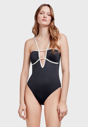 Maillot de bain noir avec un décolleté en V profond, des bretelles blanches accentuées, un tissu froncé au niveau de la poitrine et un design à cuisse haute pour une silhouette élancée.