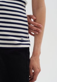 Top a righe navy e bianche in maglia a coste con una vestibilità slim. Presenta un piccolo logo vicino all'orlo, abbinato a pantaloni in denim scuri.