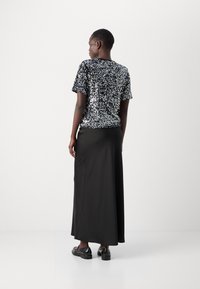 Haut à manches courtes en sequins noirs associé à une longue jupe noire ; texture lisse avec des accents scintillants ; porté avec des chaussures noires.