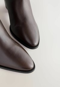 Pari nahkasaapaita tummanruskeana, kärjessä terävät varpaat ja mustat pohjat vaalealla pinnalla.