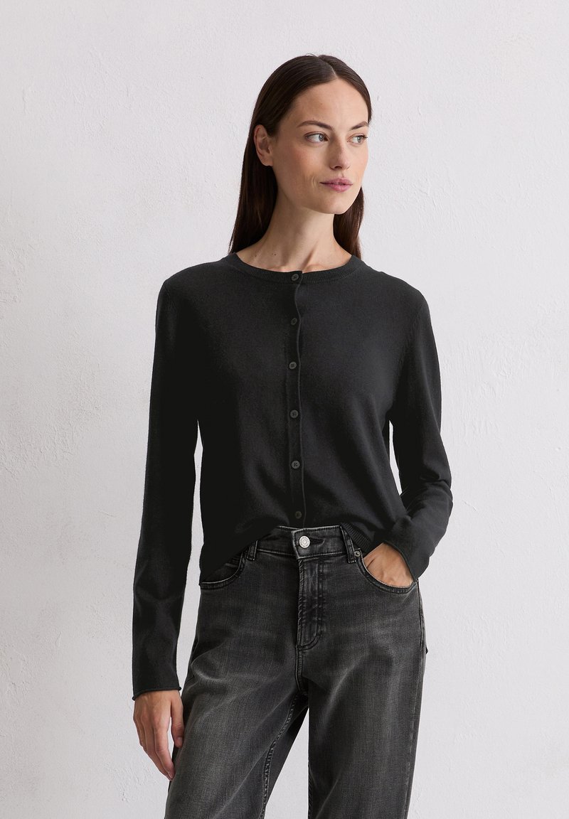 Cardigan noir avec un col rond, fermeture à boutons sur le devant et manches longues, associé à un jean gris foncé. Texture tricot lisse.