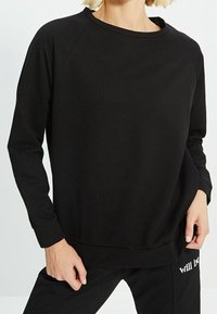 Schwarzes Sweatshirt mit langen Raglanärmeln, rundem Ausschnitt und gerippten Bündchen. Weicher Stoff mit einem entspannten, lockeren Schnitt, der minimale Designdetails aufweist.