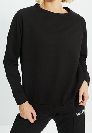 Sudadera negra con mangas raglán largas, cuello redondo y puños acanalados. Tejido suave con un ajuste relajado y holgado, con detalles de diseño mínimos.