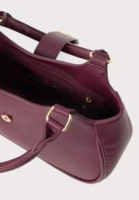 Burgundi punase sünteetiline käekott, millel on struktureeritud kuju, sile tekstuur ja kuldsete detailidega aksessuaarid. Includes sisemine luku-tasku ja tugevad sangad.