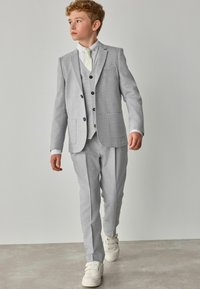 Completo grigio chiaro a tre pezzi con rever a nappe, chiusura a due bottoni e tessuto testurizzato; abbinato a una camicia bianca e una cravatta in tonalità pastello.