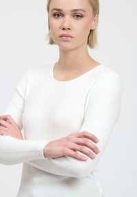 Maglietta bianca a maniche lunghe con scollo rotondo. Il tessuto ha una consistenza liscia, che mette in risalto il design aderente e i dettagli delle maniche.